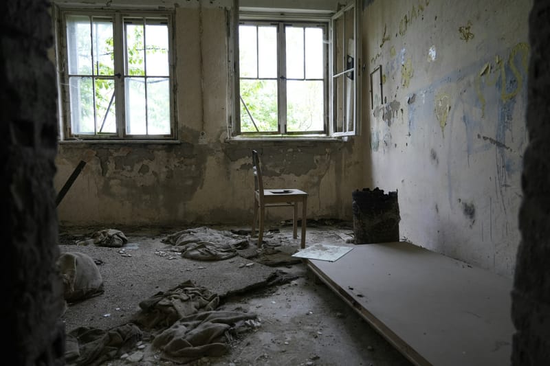A small abandoned room with graffiti on the plaster, rubble across the floor and a single chair by the window