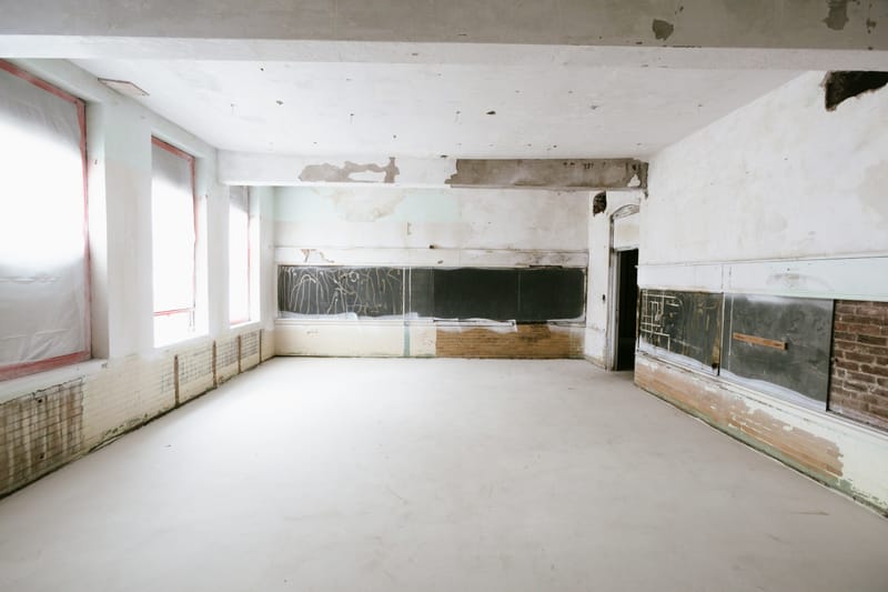 A stripped and derelict room with chalkboards still fixed to the wall, peeling plaster and a bare concrete floor