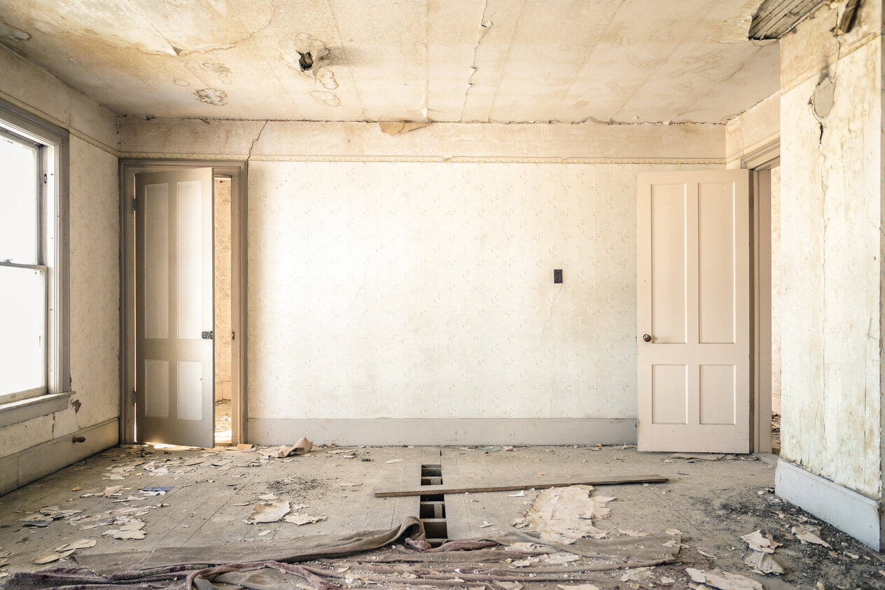 A derelict room photographed before any redesign: cracked plaster, a damaged ceiling and debris on the floor
